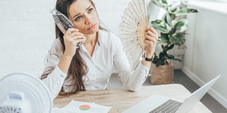 businesswoman cooling herself with electric fan, hand fan and bottle of water