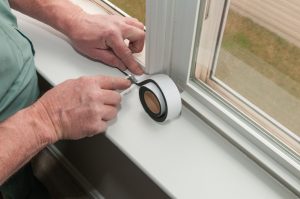 A man applying white sealing tape to a window frame