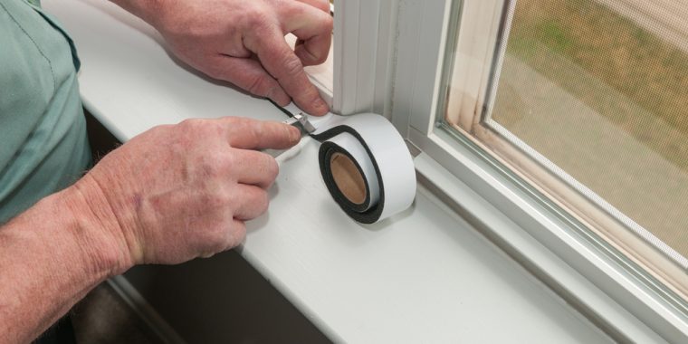 A man applying white sealing tape to a window frame