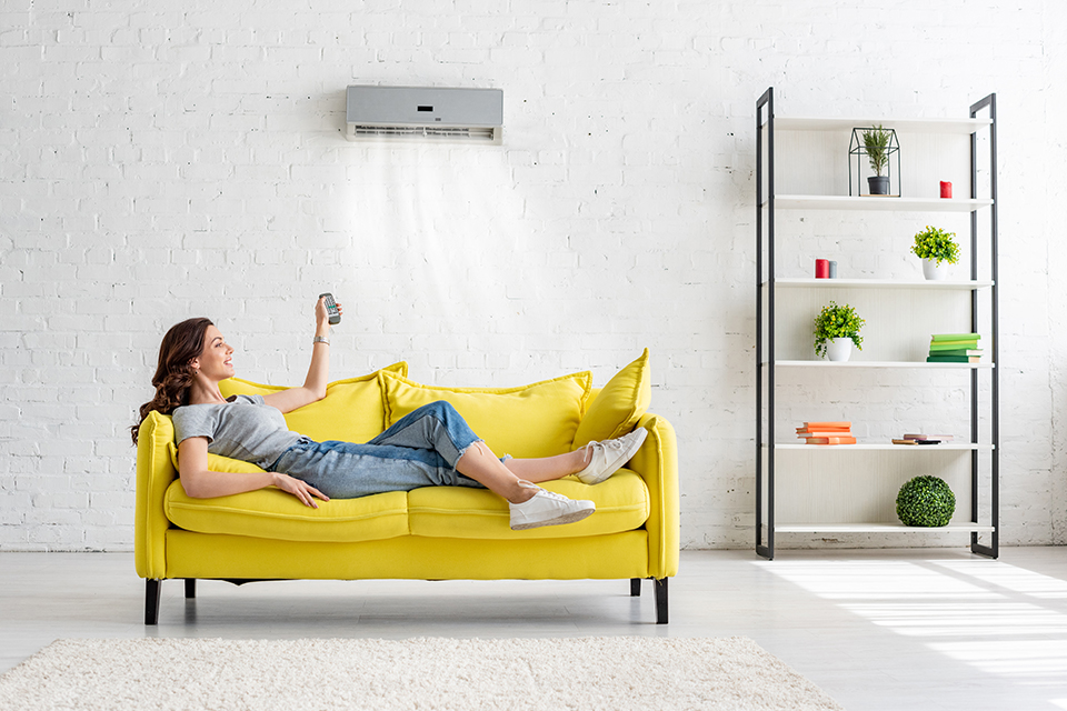 attractive young girl lying on yellow sofa under air conditioner at home
