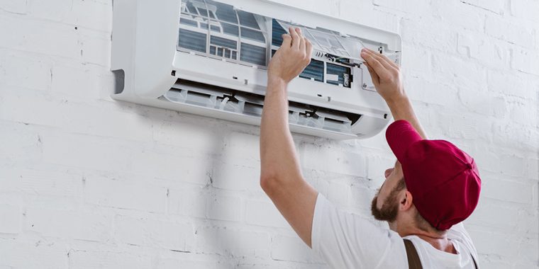 young repairman changing filter for air conditioner hanging on white brick wall
