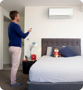 man in bedroom controlling his split system airconditioner with a remote