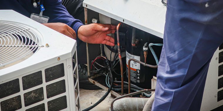 Plumbers servicing refrigerated air conditioner unit